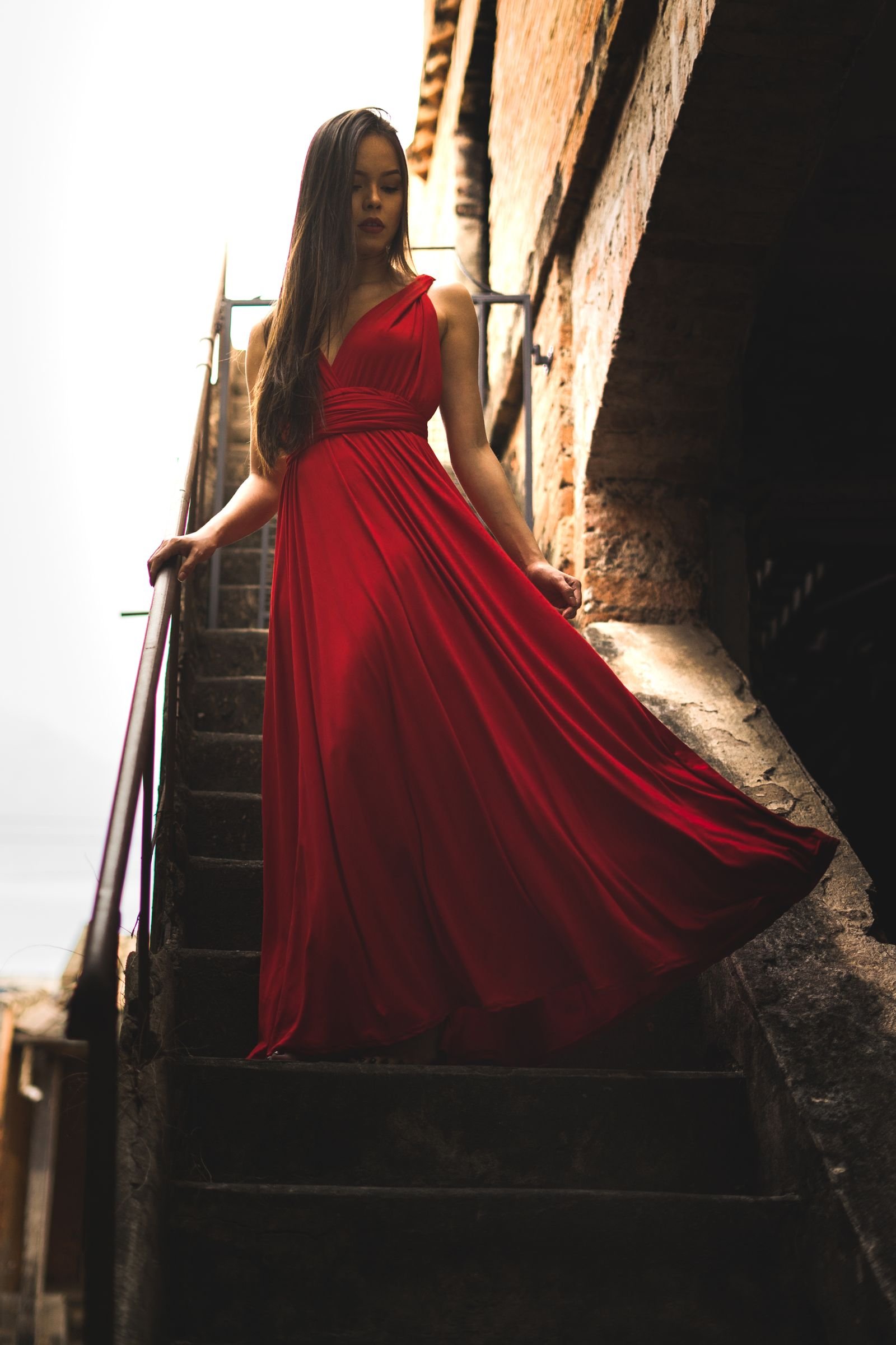 Model in a floor-length red satin gown on an outdoor stairway.